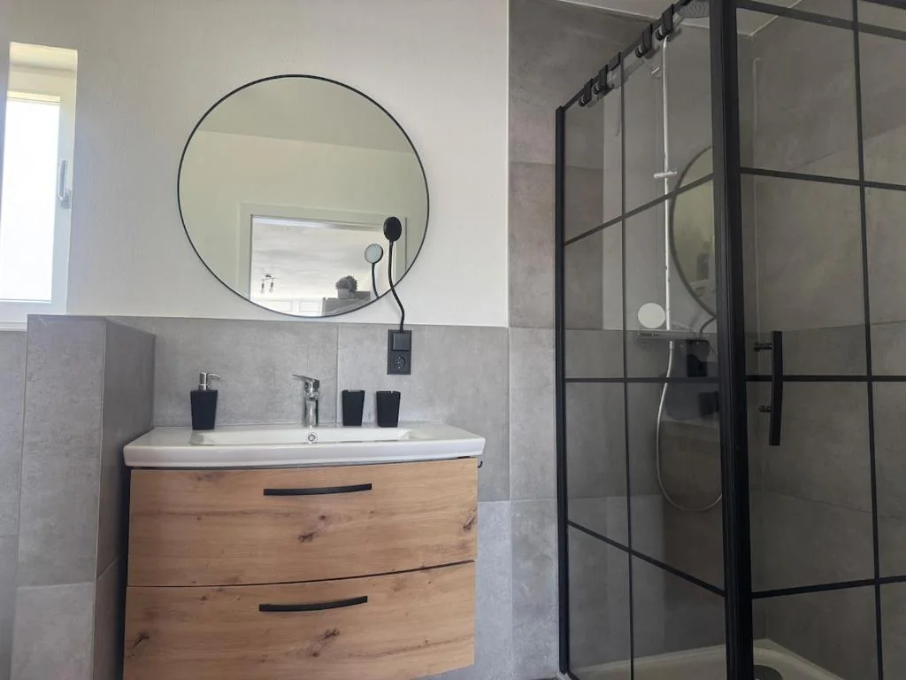Badezimmer mit rundem Spiegel und Glasdusche — Casa Daniela Donau